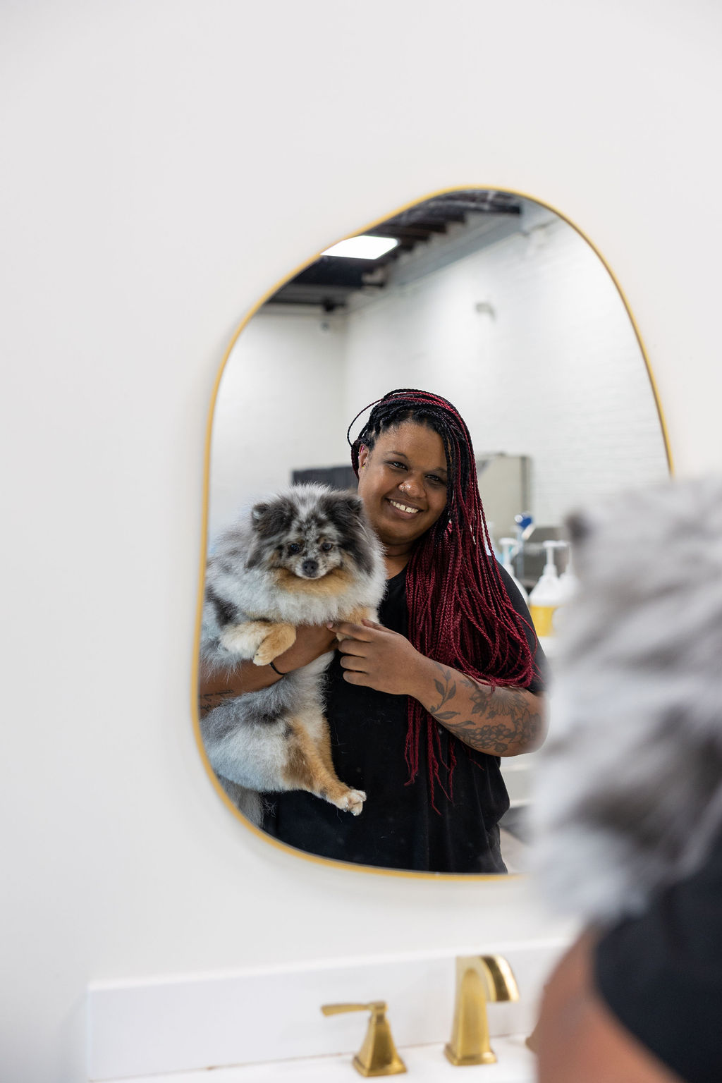 FreshCoat Grooming Bather FreshCoat Grooming bather smiling in the salon mirror while holding a fluffy blue merle Pomeranian in Charlotte, NC